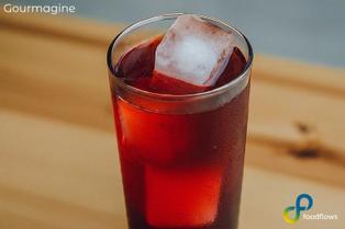 Long drink glass with foodflows coffee cherry elixir and ice cubes on a wooden table