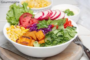 A white bowl filled with sweet potatoes, various vegetables and salads