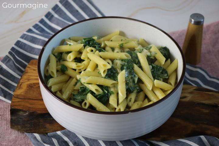 A white bowl filled with penne, chard and cheese on a dark brown wooden board