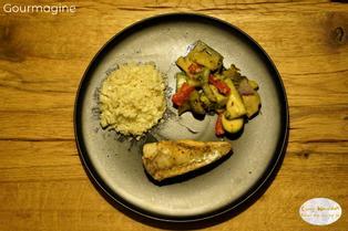 Schwarzer Teller mit Fisch, Gemüse und Blumenkohlreis auf einem hölzernen Tisch