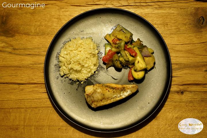 Black plate with fish, vegetables and cauliflower rice on a wooden table