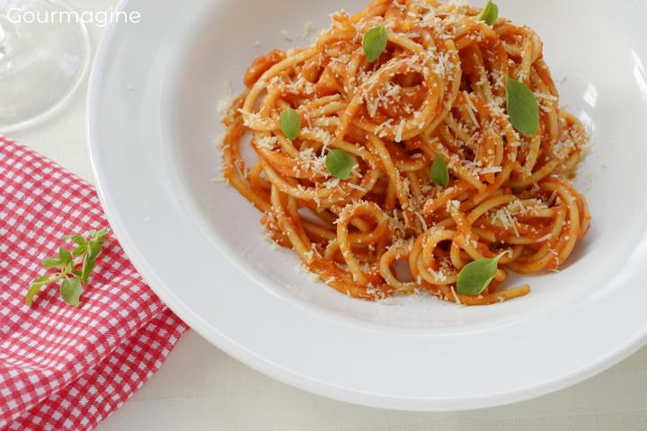 Spaghetti, Basilikum, Zwiebeln und Tomatensauce angerichtet auf einem weissen Teller neben einer roten Serviette