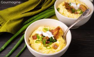 Two white bowls with yellow corn grits and red bacon on a dark table with a green napkin