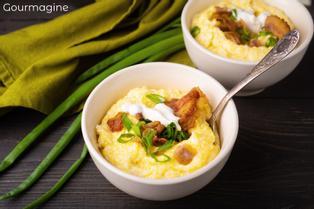 Two white bowls with yellow corn grits and red bacon on a dark table with a green napkin