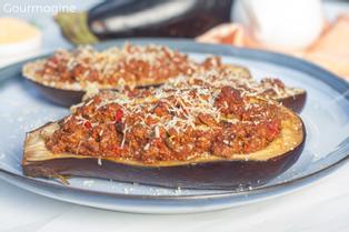 A blue plate with two baked aubergine halves that are filled with a tomato beef mixture