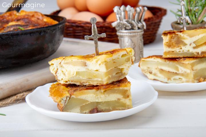 A white plate with two pieces of Spanish Tortilla held together with a toothpick in the form of a grey sword