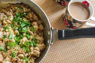 A steel frying pan with an egg mixture seasoned with green coriander leaves next to a cup with Indian chai tea