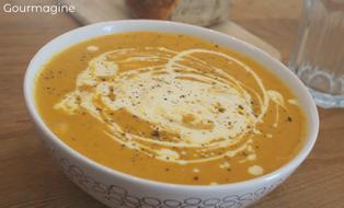 Eine weisse Schüssel gefüllt mit brauner Süsskartoffel-Rüebli-Suppe und einem Spritzer Crème Fraîche