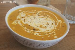 A white bowl filled with brown sweet potato and carrot soup and a drizzle of crème fraîche