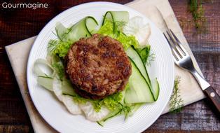 A white plate with a bed of cucumber salad topped with burger patties
