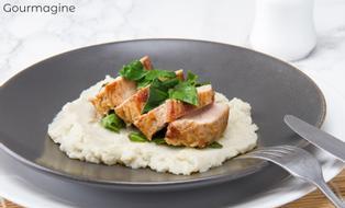 Several pieces of pork on a cauliflower puree served on a black plate