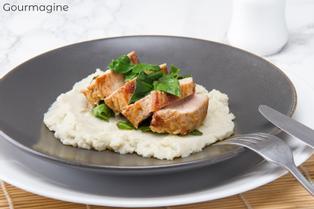Several pieces of pork on a cauliflower puree served on a black plate