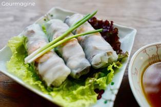 White plate with three semi-transparent Vietnamese summer rolls on a leaf of lettuce next to a bowl with brown sauce