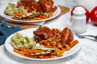 Two white plates with brown chicken pieces in a tomato corn sauce and fried carrots, courgettes and cauliflower