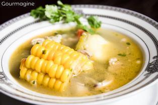 A white bowl filled with clear chicken soup and corn cobs