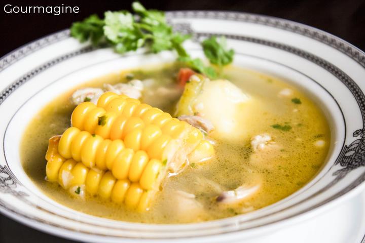 A white bowl filled with clear chicken soup and corn cobs