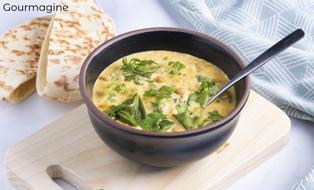 Ein Tomaten-Joghurt-Linsen-Curry angerichtet in einer schwarzen Schüssel neben zwei Pitabroten
