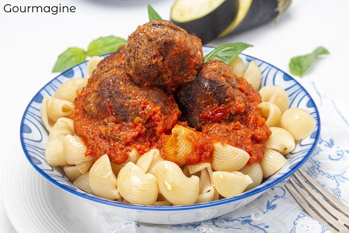 Blue bowl with ellbow pasta covered with red tomato sauce and aubergine quinoa balls on a white table