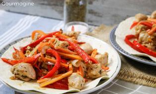A tortilla filled with chicken pieces, peppers and carrots on a plate