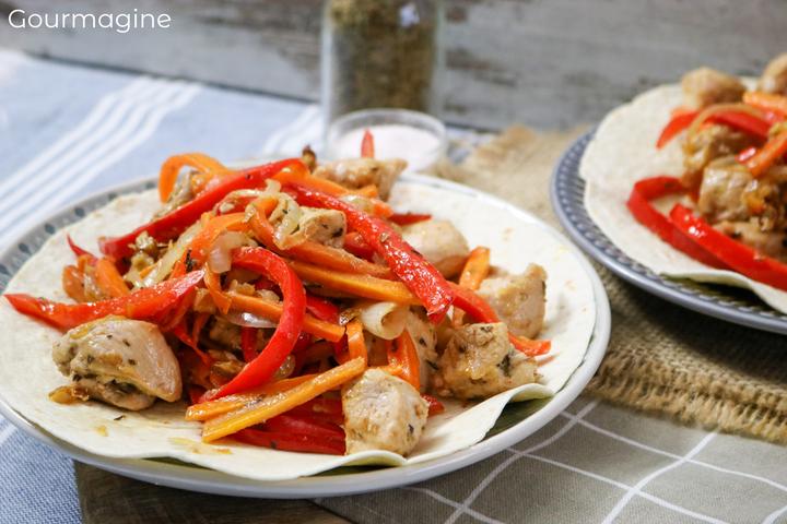 A tortilla filled with chicken pieces, peppers and carrots on a plate 