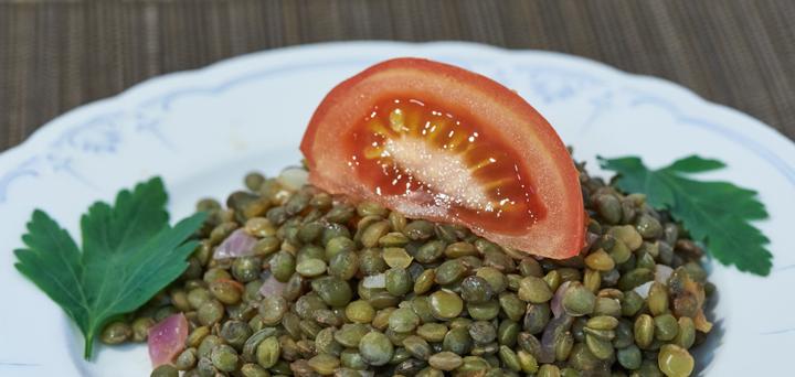 A white plate with lentils and a tomato slice