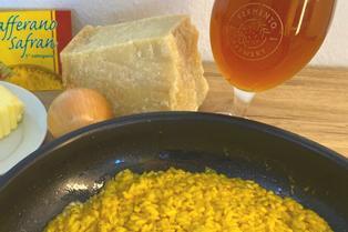 Black bowl with yellow beer risotto next to a hard cheese, safran sachet and a glass of beer