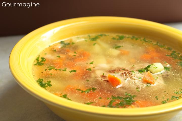 A yellow bowl filled with a soup and chicken, carrot and potato pieces