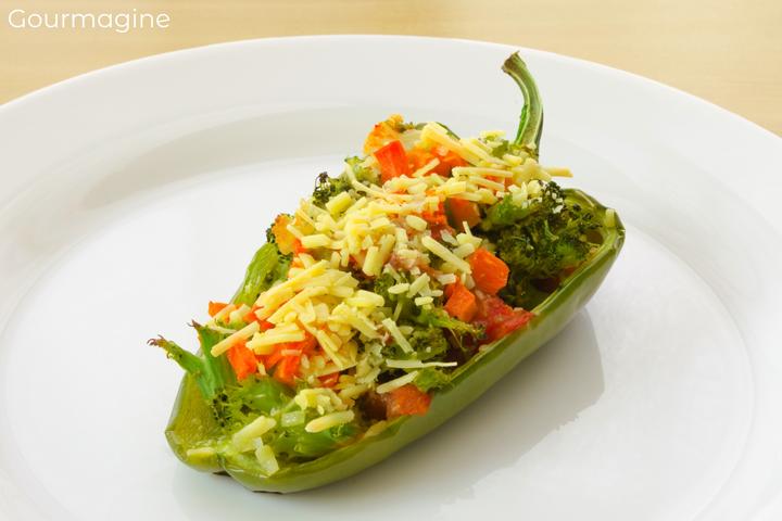 Half of a green pepper filled with broccoli pieces, carrot cubes, tomatoes and small onions covered with Parmesan cheese on a white plate