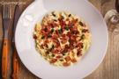 A white plate filled with cabbage salad, diced bacon and pumpkin seeds