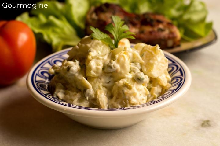 Eine Schüssel gefüllt mit Kartoffelsalat und Erbsen neben einem Teller mit grünem Salat