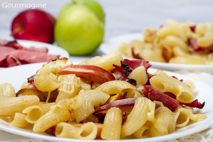 Teller mit Hörnli, Äpfeln, Fleisch und Käse und zwei Äpfel im Hintergrund