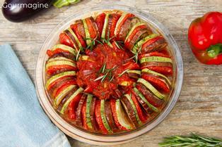 Round baking form with baked aubergine, courgette and tomato slices arranged in concentric circles and topped with tomato sauce