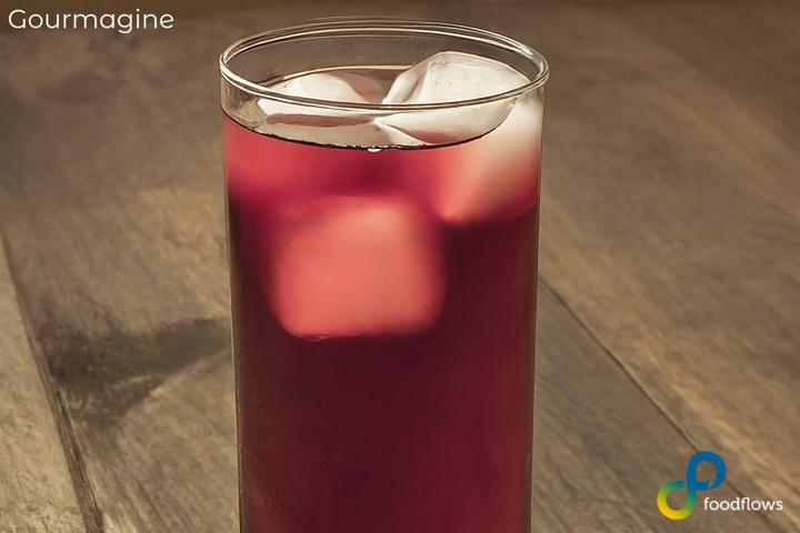 Long drink glass with foodflows coffee cherry elixir and ice cubes on a wooden table