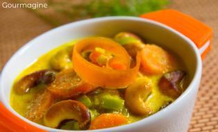 An orange and white bowl filled with carrots, leeks, parsnips and cashews in a curry sauce