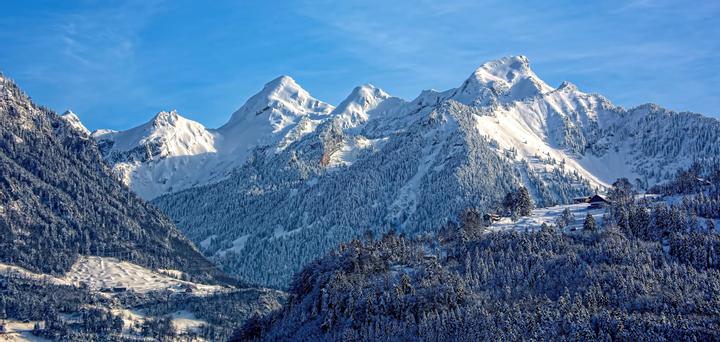Bild einer winterlichen Naturlandschaft mit eingeschneiten Wäldern und Schneebergen