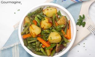 A white bowl with roasted green beans, potatoes, carrots and onions