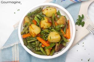 A white bowl with roasted green beans, potatoes, carrots and onions