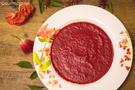 A decorated white plate filled with curried beetroot soup and decorative rose petals