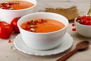 White bowl with red gazpacho and tomatoes in the background