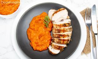 A roasted chicken breast cut into several pieces served with carrot puree on a black plate