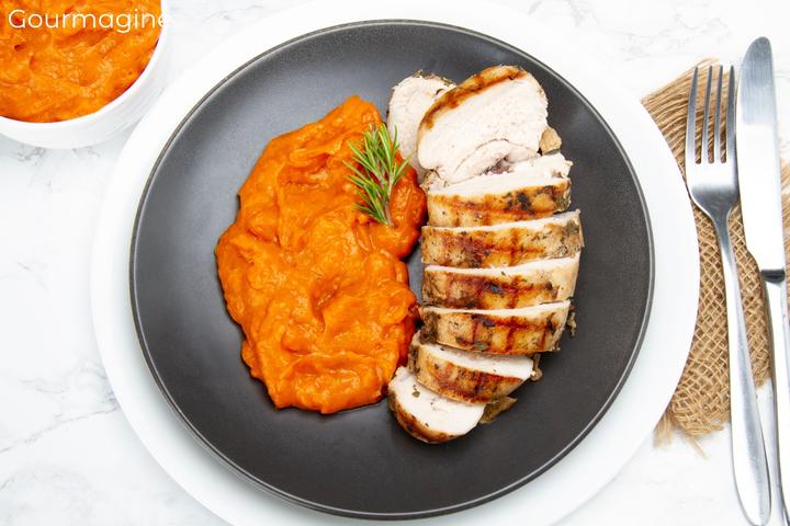 A roasted chicken breast cut into several pieces served with carrot puree on a black plate