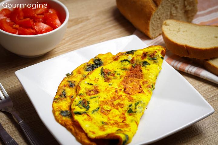 Yellow and green chard omelette on a white plate next to a bowl with tomato wedges and slices of bread