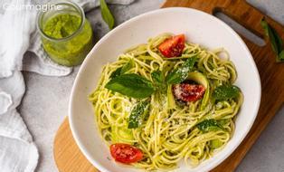 A white bowl filled with spaghetti with pesto and tomatoes