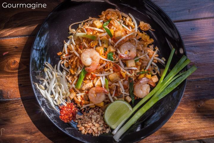 Black bowl with cooked noodles, tofu, prawns, sprouts and peanuts on a wooden table