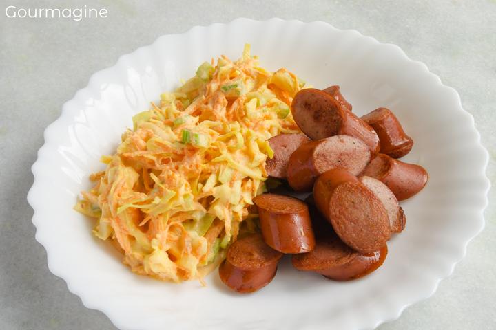 Kabis-Rüebli-Salat und ein geschnittenes Wienerli angerichtet auf einem weissen Teller