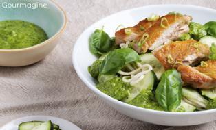 Eine weisse Schüssel mit Nudeln, Poulet und Gurken neben einer Schüssel mit grüner Sauce und einem Teller mit geschnittenen Gurken