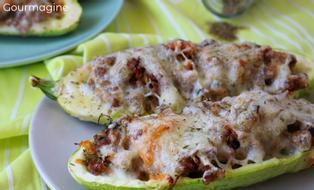 Two halved, hollowed out courgettes filled with minced meat and carrots and topped with cheese on a light blue plate