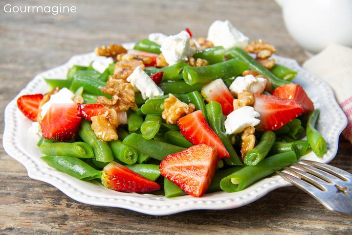 Green beans with walnuts, feta and strawberries served on a white plate