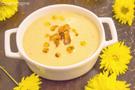 Eine Blumenkohl-Kichererbsen-Suppe in einem weissen Topf angerichtet und mit gelben Blumen dekoriert