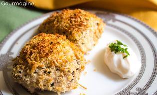 Zwei Pouletstücke mit einer Käse-Basilikum-Kruste angerichtet auf einem weissen Teller